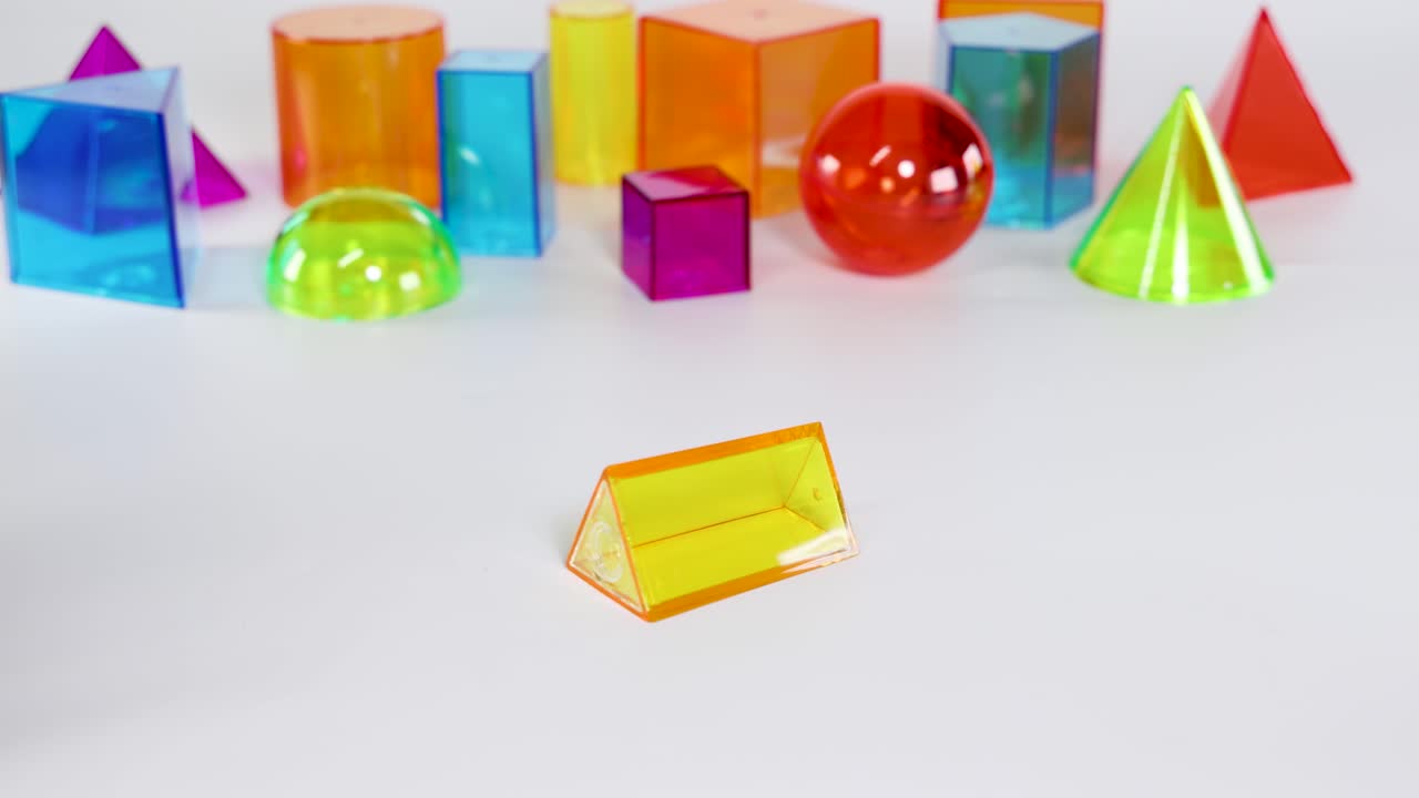 A hand interacts with colorful 3D geometric shapes on a white surface under bright lighting