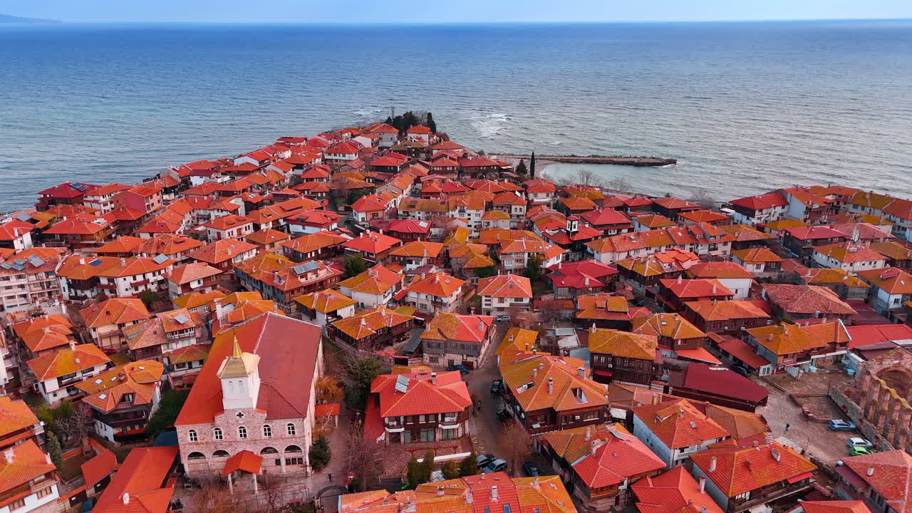 Tomada de ângulo alto da ponta da cidade com o mar ao fundo. Vista do fim de uma península apresentando telhados vermelhos, uma igreja e o mar aberto.