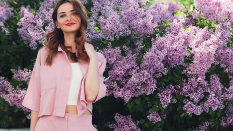 woman in pink suit posing among lilacs