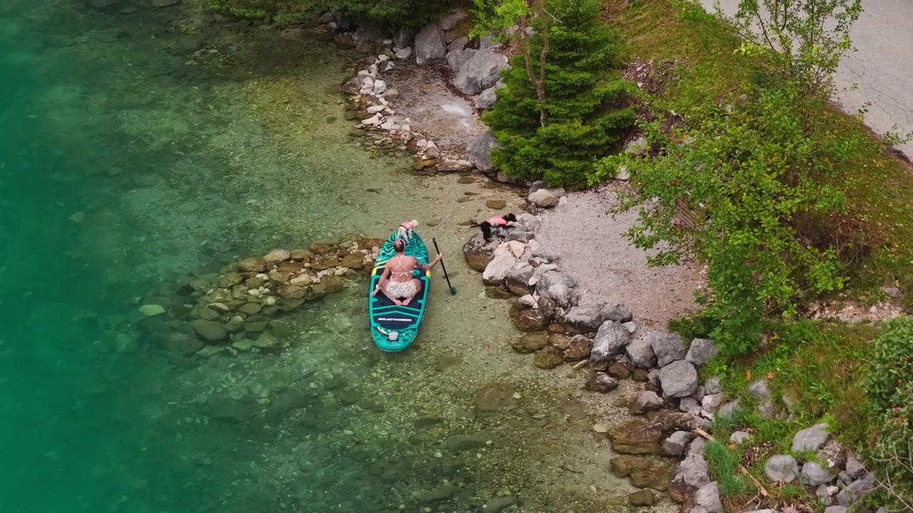 Una donna fa paddleboard vicino alla riva rocciosa del Lago Achensee in Tirolo, Austria, con acqua limpida del lago e costa rocciosa visibili - ripresa con drone.