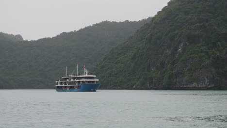 Blue-Cruise-Ship-Passing-On-Mountains-background-In-Ha-Long-Bay,-Northeast-Vietnam