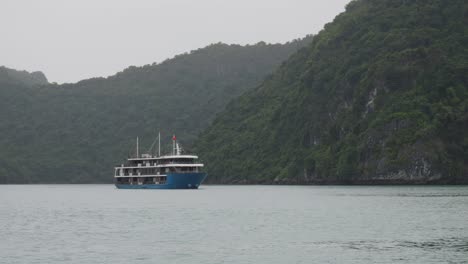 blue cruise ship passing on mountains background in ha long bay, northeast vietnam