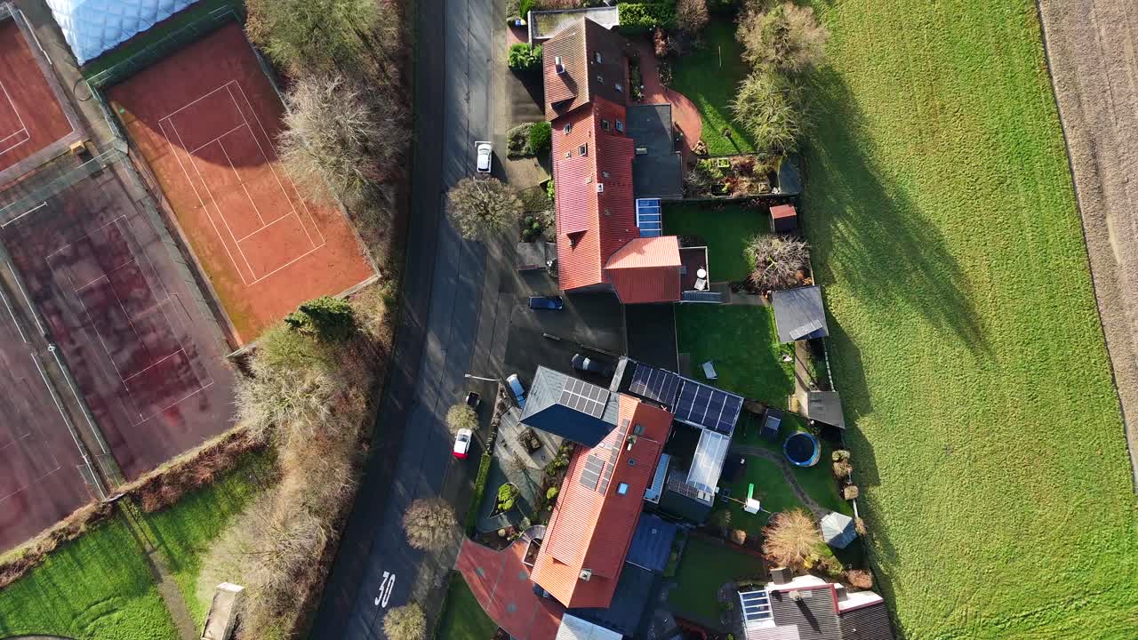 Aerial flyover Single family houses with solar panels on roof be tennis field during sunny day. Fall season in America near rural countryside. Car on street in american neighborhood community.