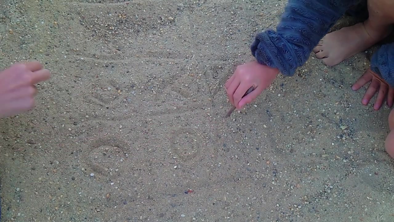 Una ripresa statica ravvicinata dall'alto mostra un bambino che disegna una linea vincente attraverso i cerchi in una partita a tris nella sabbia grossolana a Flava Beach a BudaPart, Budapest, Ungheria.