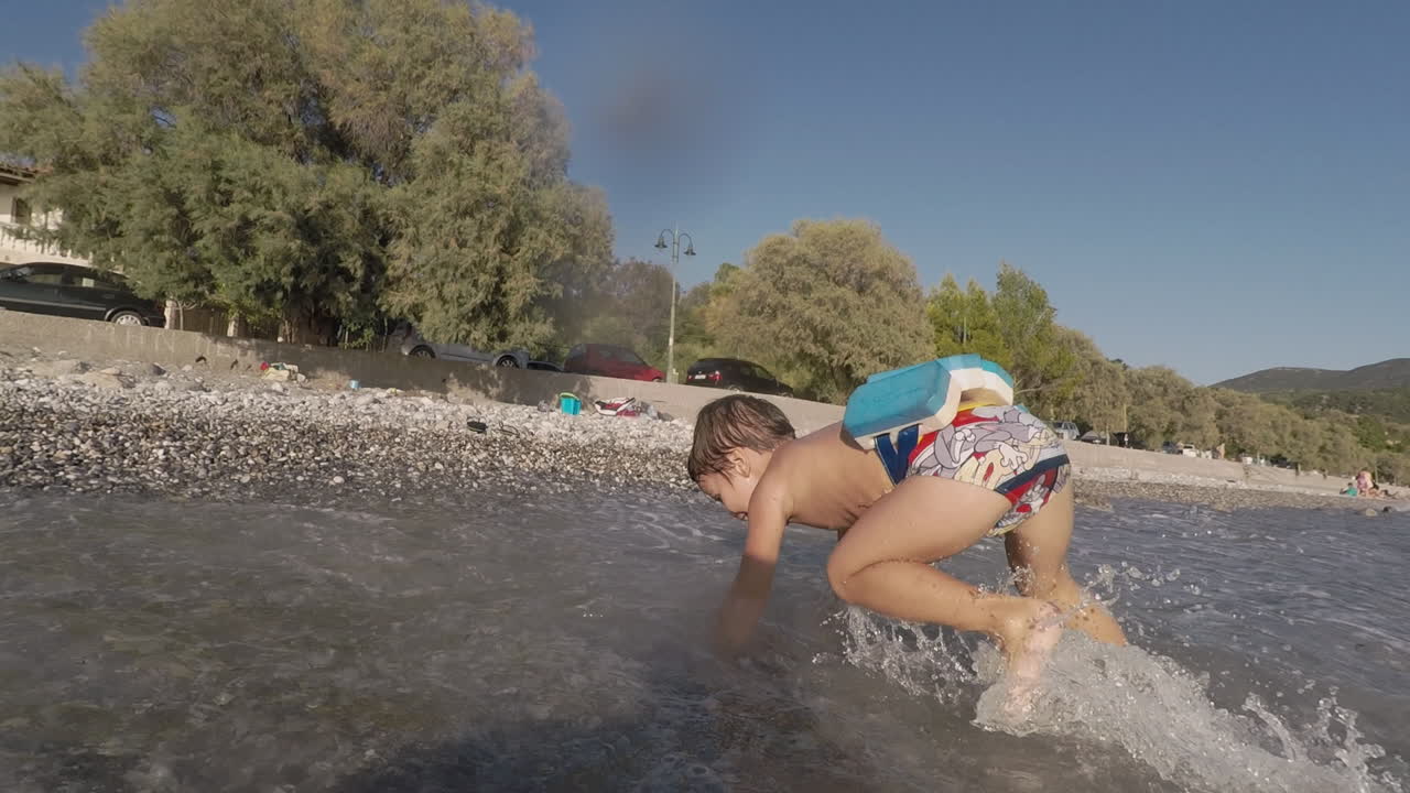 imágenes de un niño de dos años jugando con olas en la playa de santova, kalamata, grecia