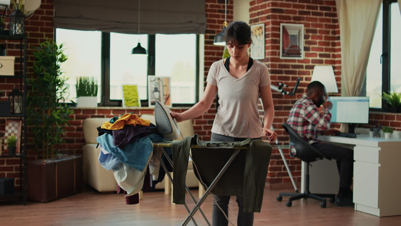 Female person ironing blouse in apartment after doing laundry