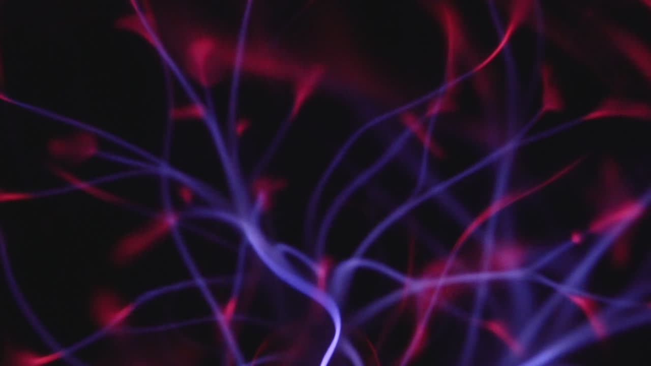 Filamenti di plasma incandescente si estendono dal centro di una sfera di plasma, emettendo vivaci archi elettrici viola e rossi su uno sfondo scuro