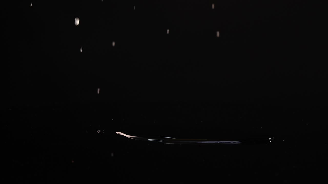 Lemon slices fall and settle on a glossy black surface, creating splashes and reflections under bright lighting