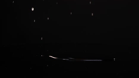 lemon slices fall and settle on a glossy black surface, creating splashes and reflections under bright lighting