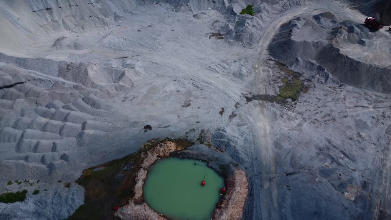Svepande drönarfilm från luften fångar ett vidsträckt grus- och granitbrott i Abuja, Nigeria. Grova texturer och neutrala toner dominerar i mjukt dagsljus. Drönaren drar sig tillbaka för att avslöja en grönskande damm.