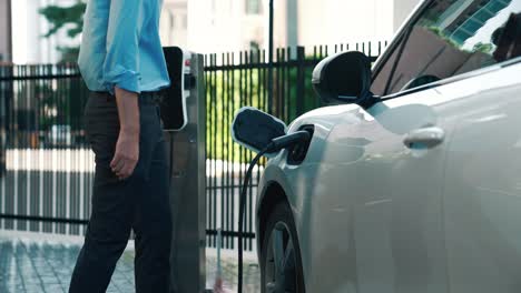 el hombre de negocios conecta el enchufe del cargador progresivo de la estación de carga a su ev.