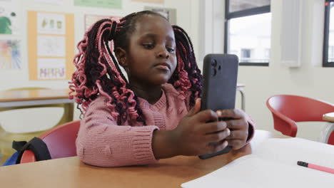 in classroom, young girl using smartphone, focusing intently on screen, at school
