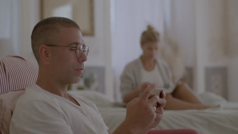 Man-playing-phone-while-his-wife-reading-book-in-morning-at-home