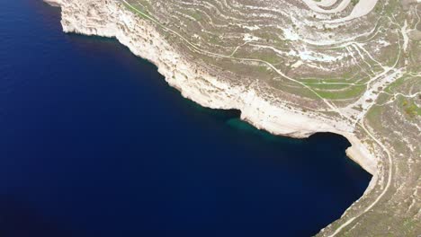 Stunning-aerial-drone-video-from-the-Maltese-countryside,-at-midday,-flying-over-the-natural-bay-and-caves-towards-the-land