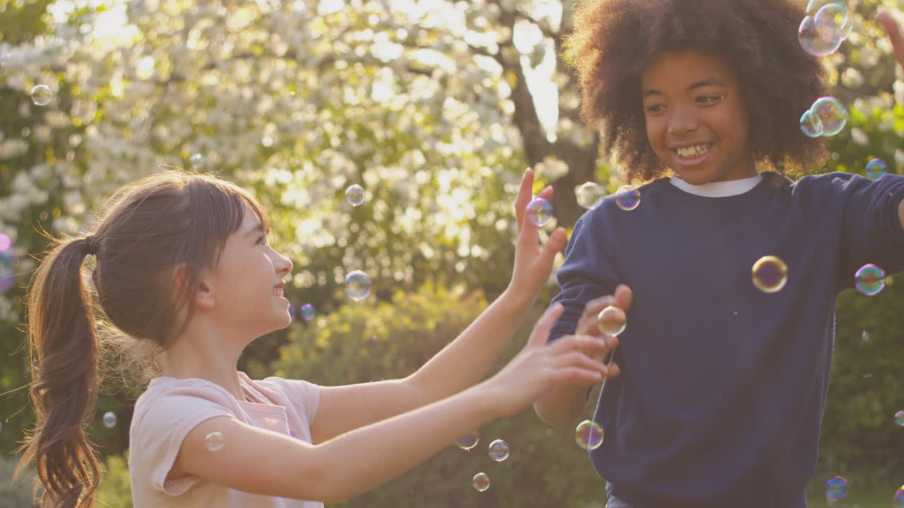 Lachende jongen en meisje buiten die plezier hebben met bellen blazen in de tuin