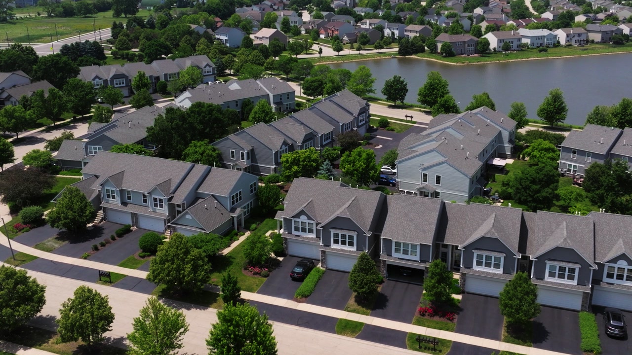 American suburban multifamily homes with green yards and clean roads along lake, idyllic neighborhood no people nobody around, aerial establish
