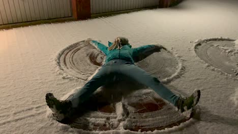 primer plano: chica con ropa de invierno haciendo ángeles de nieve en la nieve fresca en la carretera durante la noche