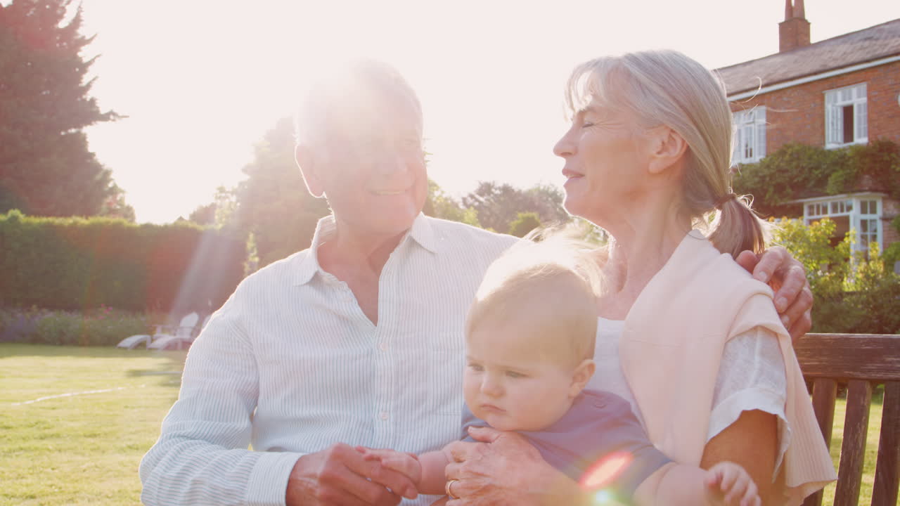 бабушка и дедушка сидят на сиденье в саду с маленьким внуком