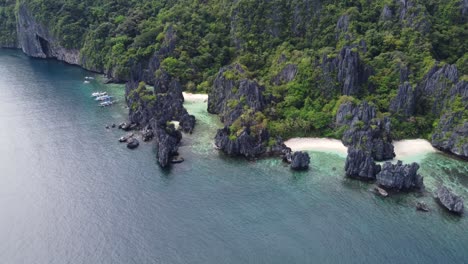 Aerial-panorama-wide-shot-:-descending-forward-towards-Hidden-Beach,-a-tropical-paradise-gem,-shallow-white-sand-crystal-clear-lagoon-between-karst-cliffs-and-part-of-Island-Hopping-Tour-C,-El-Nido