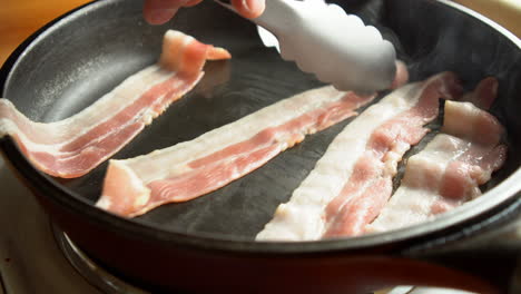 hombre chef cocinando para el desayuno un increíble tocino crujiente, rico en grasa y color, chisporroteando y fumando en una sartén caliente