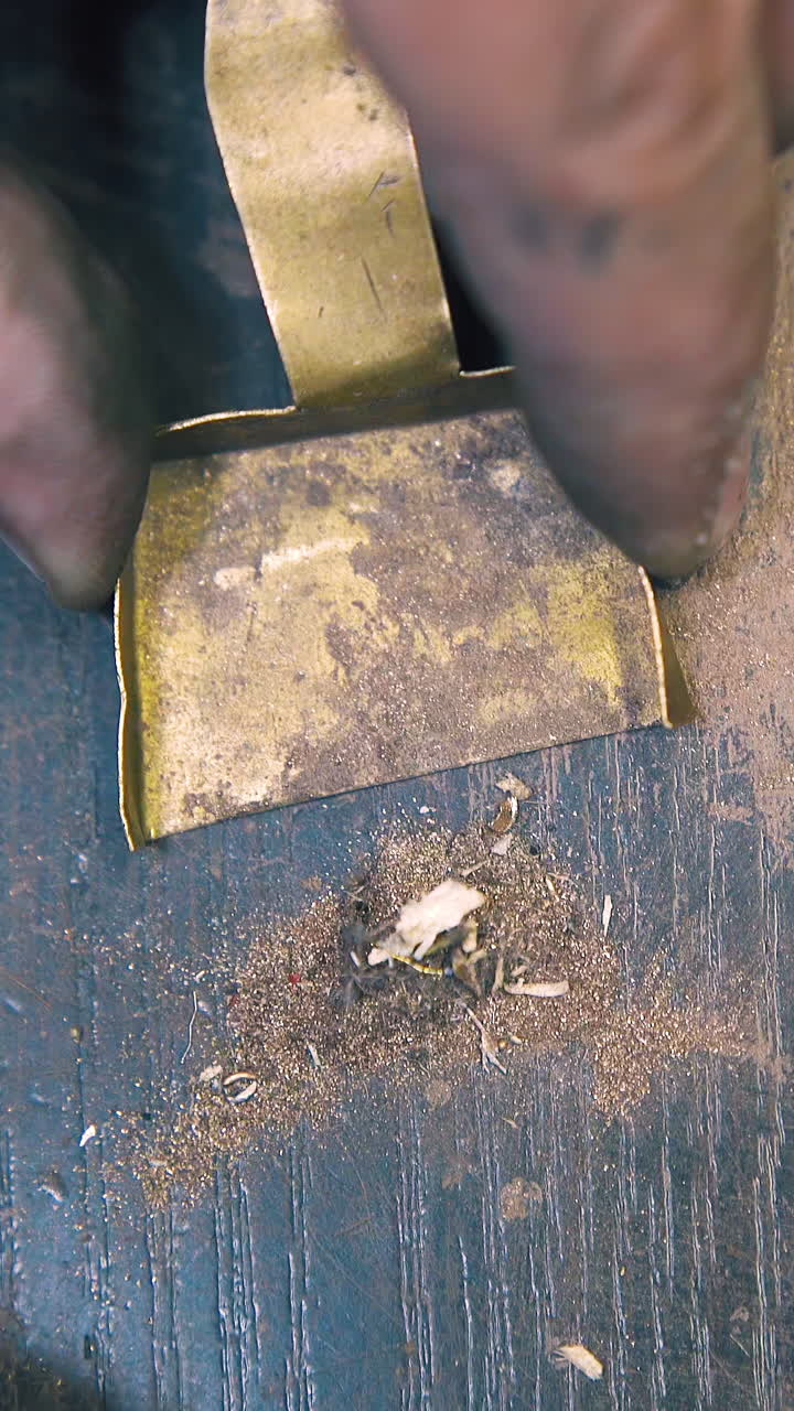 CU: professional goldsmith brushes metal dust into small shovel from wooden table at bright light close upper view