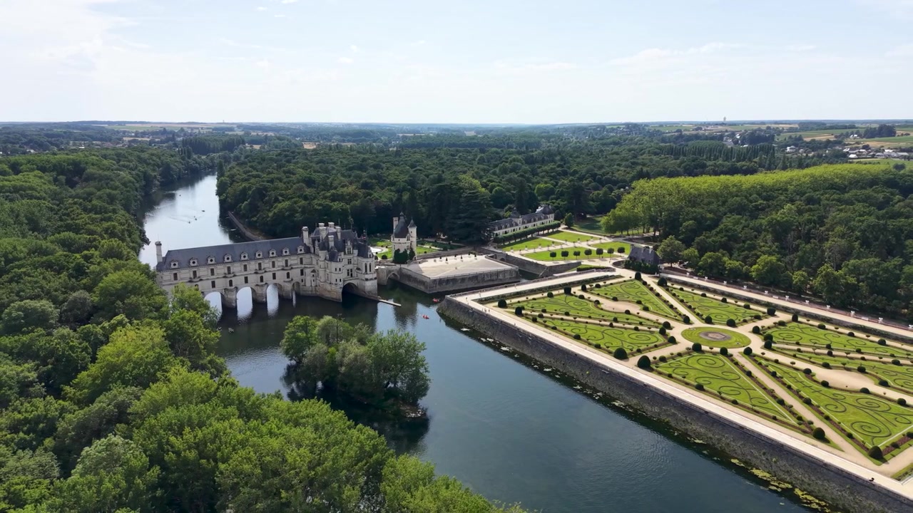 Panorama aéreo cinematográfico con dron del Castillo de Chenonceau que se extiende sobre el río Cher, mostrando los jardines franceses formales, la arquitectura renacentista y los bosques circundantes