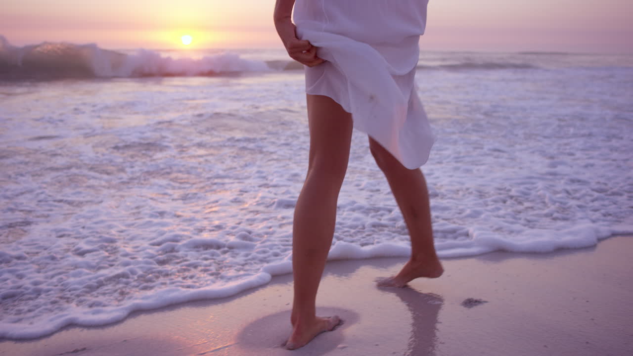 cosecha hermosa mujer levantando vestido blanco caminando a lo largo de la costa en la playa al atardecer en cámara lenta dragón rojo