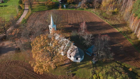 Die-Aufsteigende-Drohnenaufnahme-Fängt-Eine-Historische-Landkirche-Ein,-Die-Von-Feldern-Und-Wäldern-In-Herbstlicher-Schönheit-Umgeben-Ist