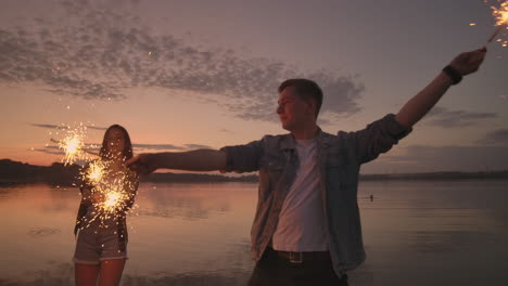 Eine-Gruppe-Befreundeter-Männer-Und-Frauen-Feiert-Den-Feiertag-Fröhlich-Am-Strand-Mit-Wunderkerzen-Und-Feuerwerk.-Zeitlupen-Nachtparty-Strandparty.