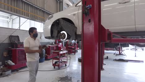 dirty latin male mechanic working on the suspension of a white car without wheel at a workshop station in mexico latin-america