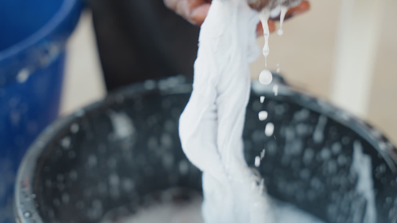 Primo piano di una scena di lavaggio di tessuti. Scena domestica che mostra mani che puliscono accuratamente un tessuto. Esame ravvicinato di mani che puliscono un panno bianco con acqua in un ambiente domestico durante le ore serali