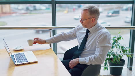 businessman wears neatly white shirt and drinking coffee near big window with city view looking away.