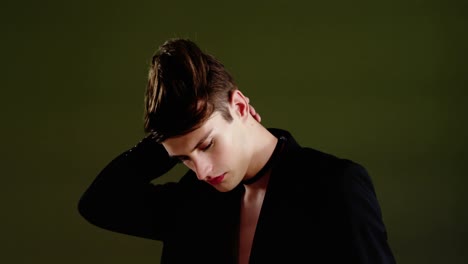 androgynous man in blazer posing against black background