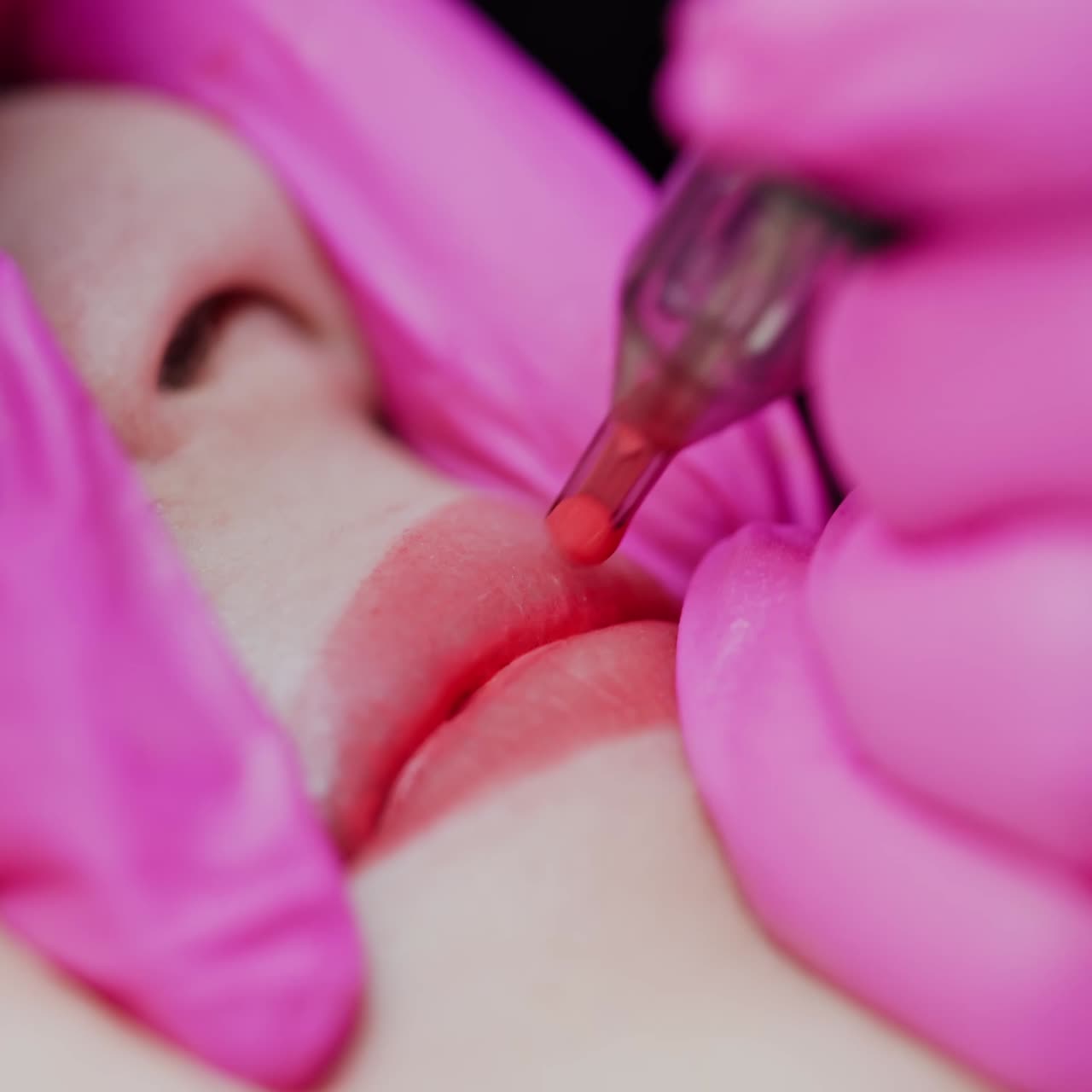 Lips tattoo. Master in pink sterile gloves applying permanent make-up on lips with a special equipment. Plastic medicine and cosmetology. Close-up.