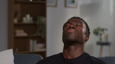 close up of unhappy and depressed young man sitting on sofa at home closing eyes