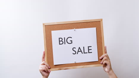 woman's hand shows the paper on board with the word big sale in white studio background with copy space