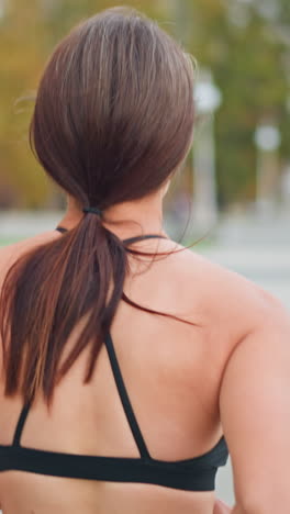 Back view of lady in black neck top running along park path with blurred background showing trees and bench, promoting outdoor fitness and healthy lifestyle