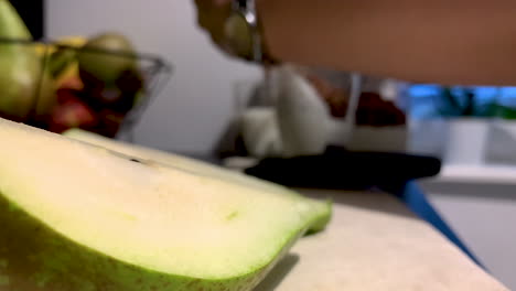 the girl is holding a knife in her hand and cutting a pear on a wooden board, next to her there are blurred glasses of yoghurt