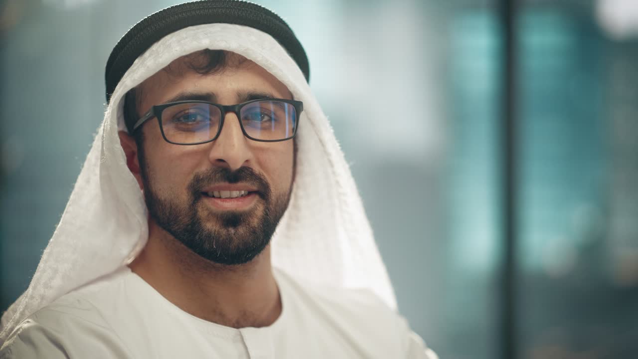 retrato de un exitoso empresario árabe en traje tradicional sonriendo suavemente, usando gafas, kandura blanca y agal negro manteniendo un ghutra en su lugar. concepto de empresario árabe saudí, emiratí.