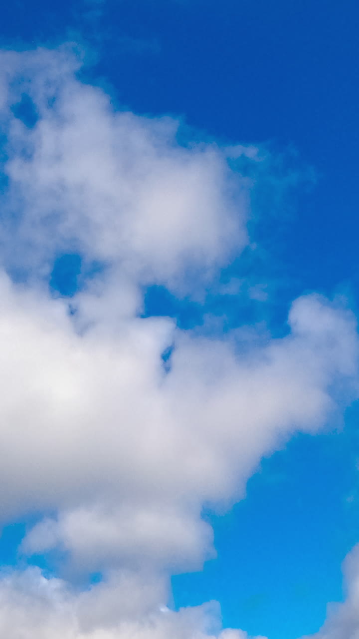 Beautiful azure sky in summer with white clouds. Cumulus cloudscape formation. Low angle view. Timelapse. Vertical video