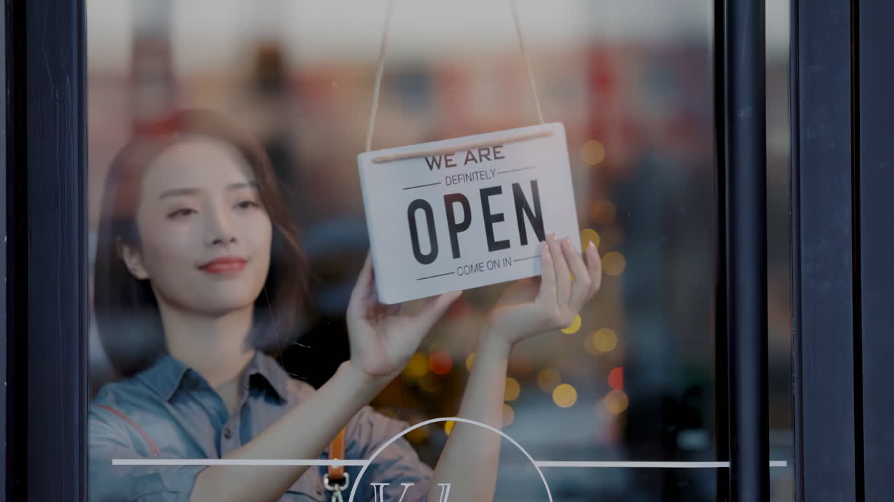 Beautiful waitress or Shopkeeper in apron hanging sorry we are closed sign on front door smiling looking outside informing people of workday end. The end of the working day. Working hard, being tired