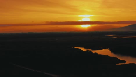 aerial drone footage of the sun rising above the pine tree forest in the iconic maremma nature park in tuscany, italy, with a dramatic cloud sky above the savannah lagoon