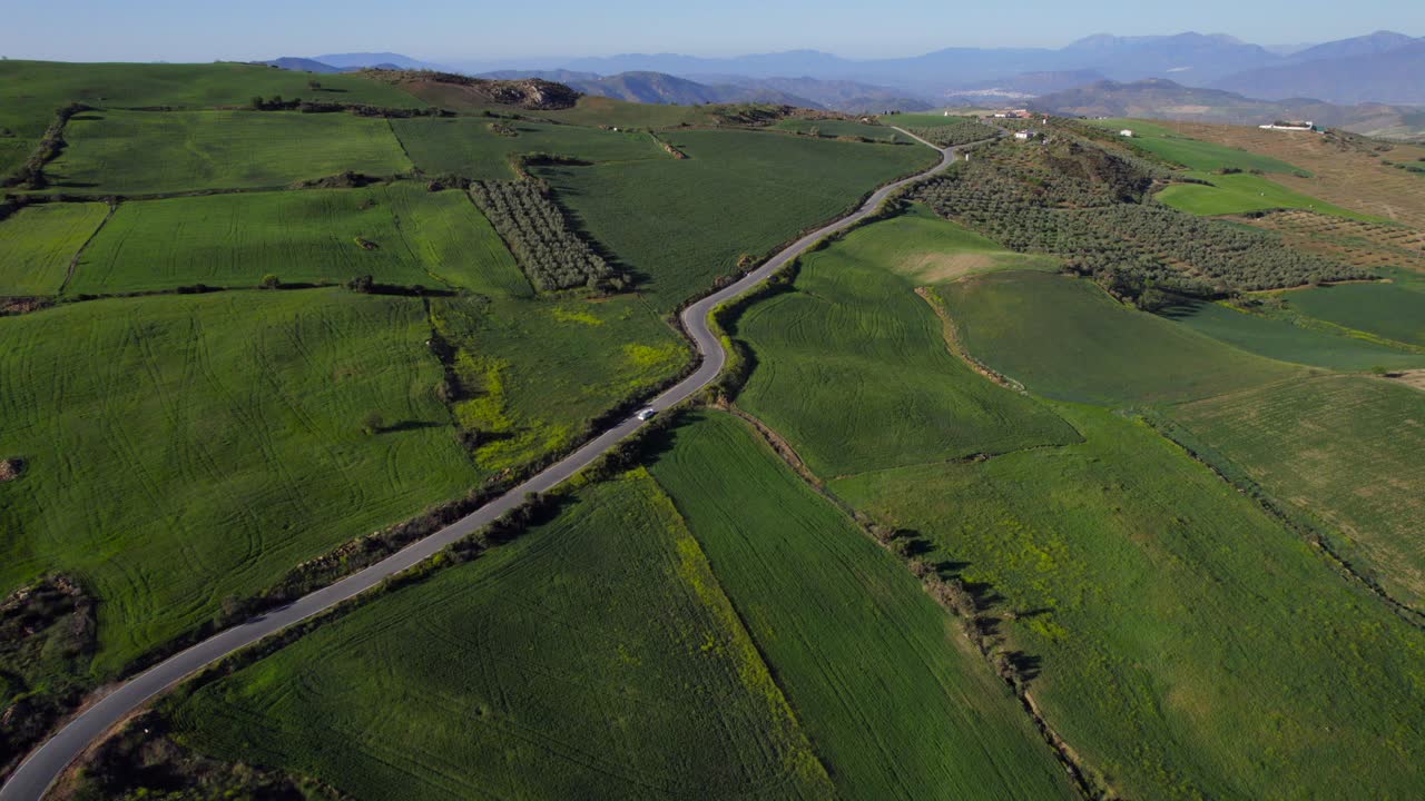 vista aérea de un vehículo solitario que viaja a lo largo de una carretera estrecha rural entre colinas verdes y tierras de cultivo