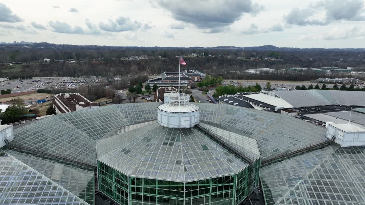 Inquadratura aerea del tetto del centro congressi di Nashville con una grande bandiera americana, che mostra l'architettura moderna, il design in vetro e il paesaggio urbano circostante sotto un cielo nuvoloso. Città patriottica degli Stati Uniti