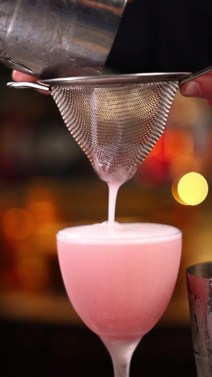 Barman che filtra un cocktail rosa in un bicchiere
