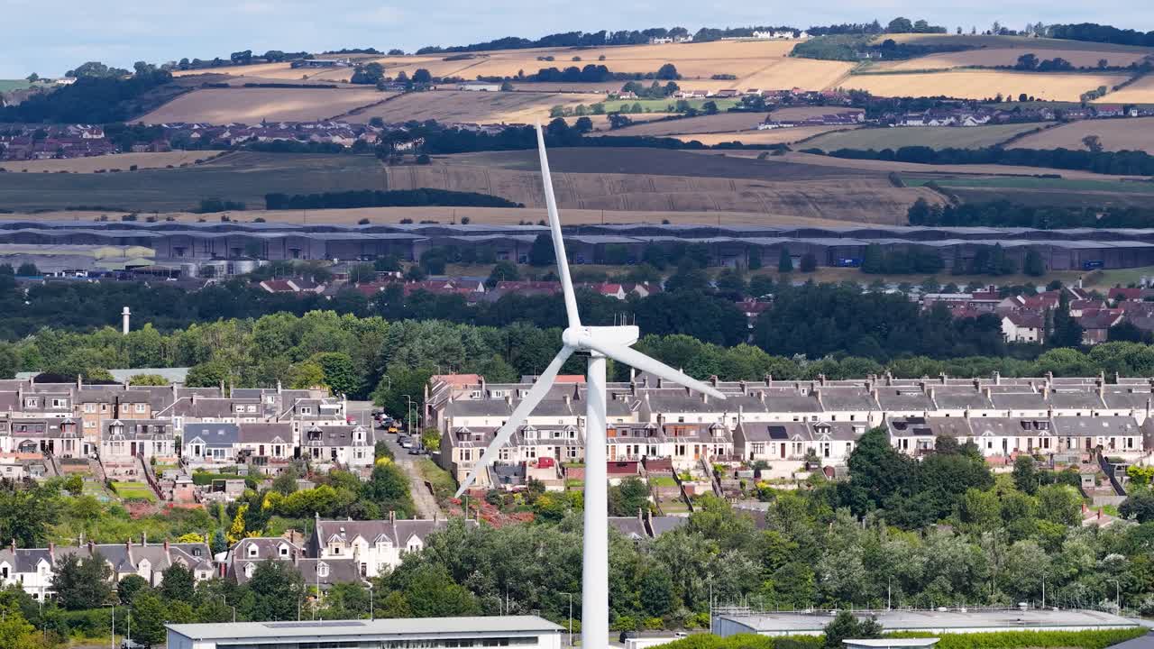 Large wind turbine spins steadily above suburban Dundee, Scotland, under bright daylight, static camera