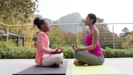 happy african american daughter and mother practicing yoga in garden, slow motion