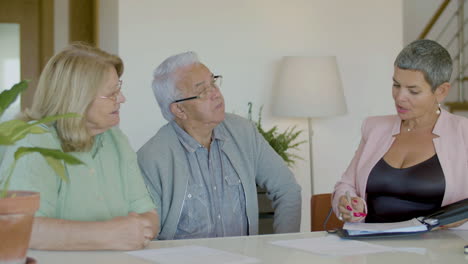 Female-realtor-sitting-at-table,-talking-with-clients-and-discussing-details-of-the-contract