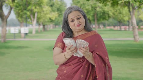 una anciana india alegre contando dinero en el parque
