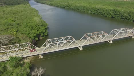 una camioneta roja de época cruza un puente de metal, seguimiento aéreo, argentina